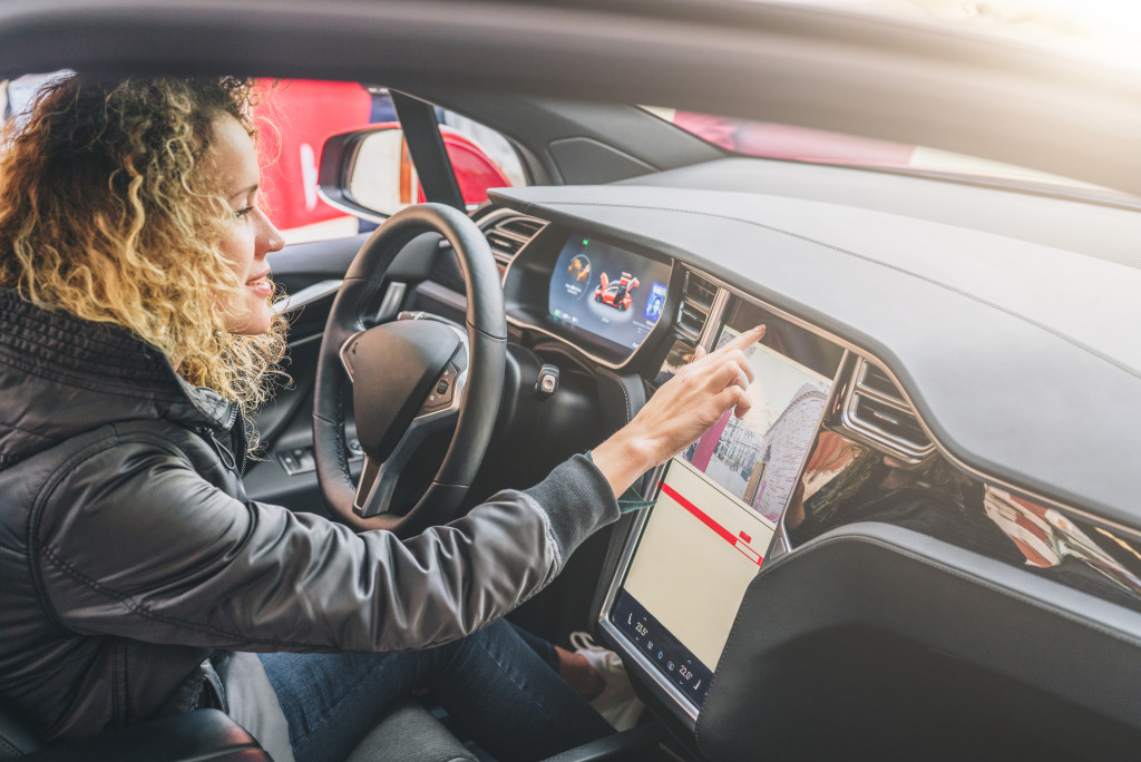 Young woman sits behind wheel in car and uses an electronic dashboard, tablet computer. Girl is traveler looking for a way through navigation system.