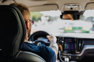 backseat view of a man driving a car, with hands on the wheel
