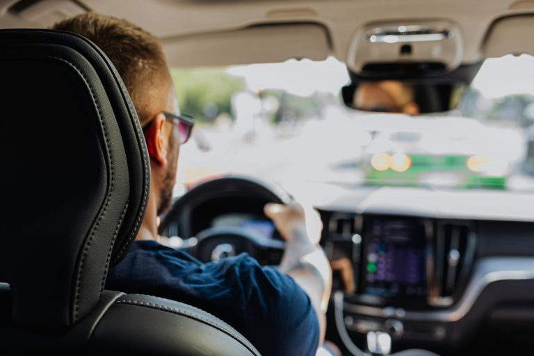backseat view of a man driving a car, with hands on the wheel
