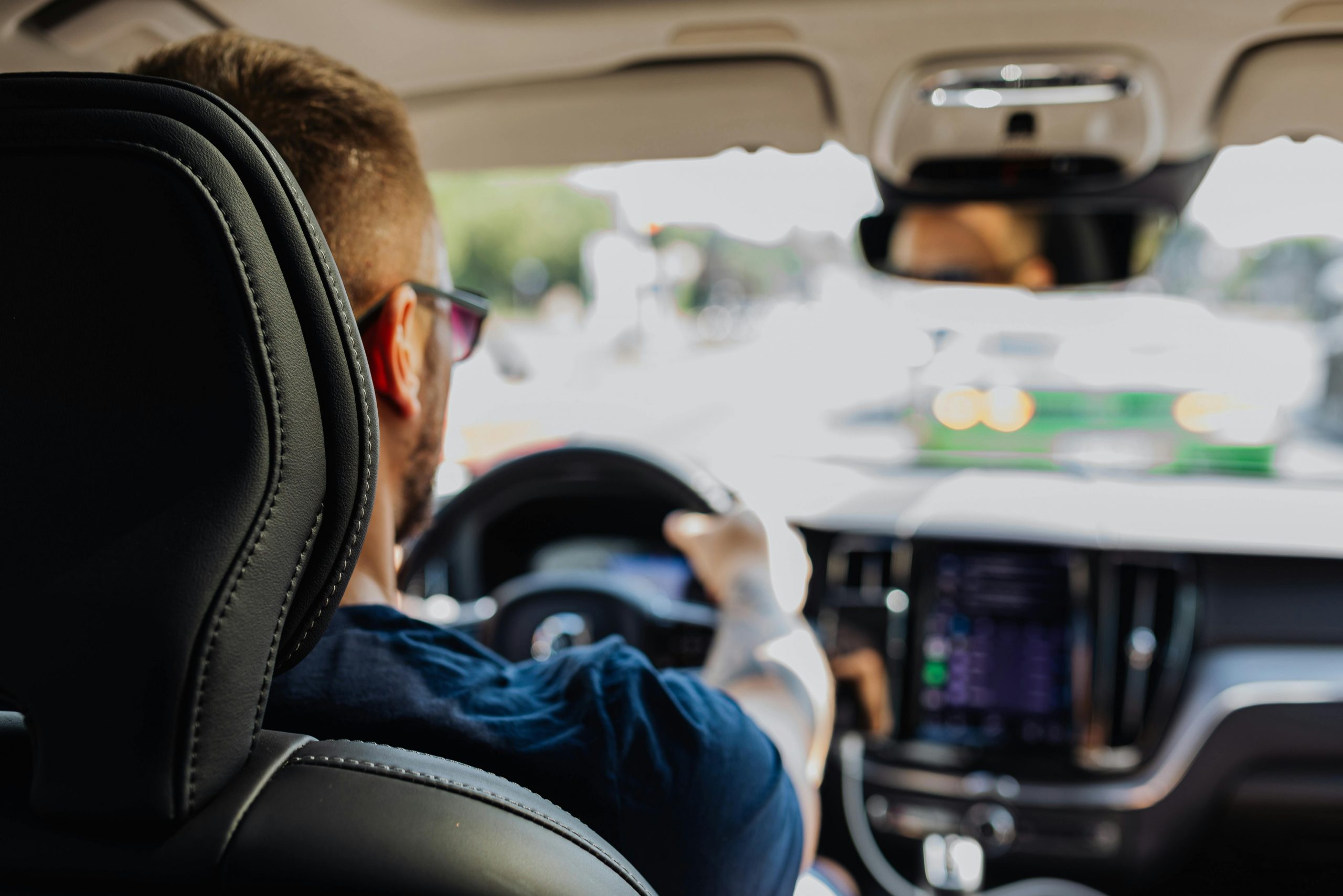 backseat view of a man driving a car, with hands on the wheel